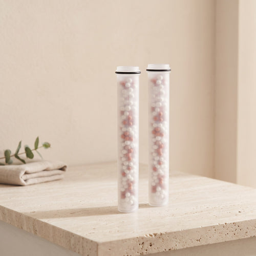 Illustration: two Driftrain refill cartridges standing on a travertine bathroom ledge (AI-made image)